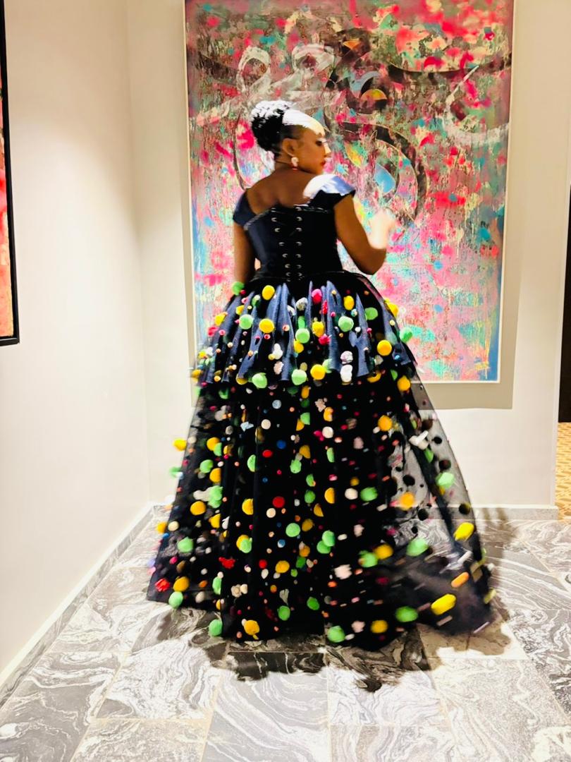 Black corseted pom-embellished ball gown photographed before a colourful abstract painting