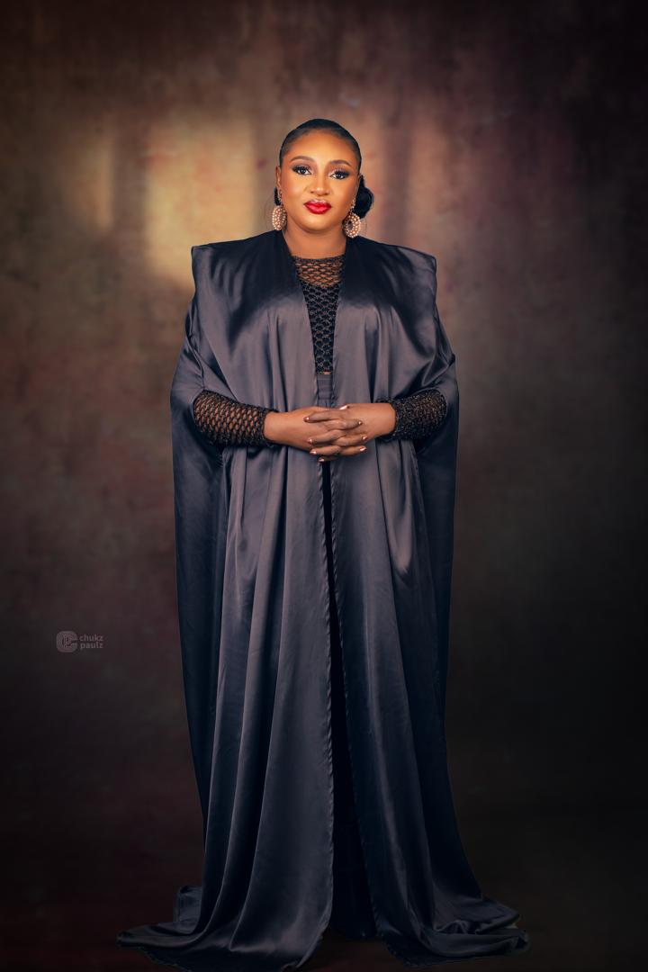 Ebere standing in a dramatic floor-length black cape gown with mesh sleeves
