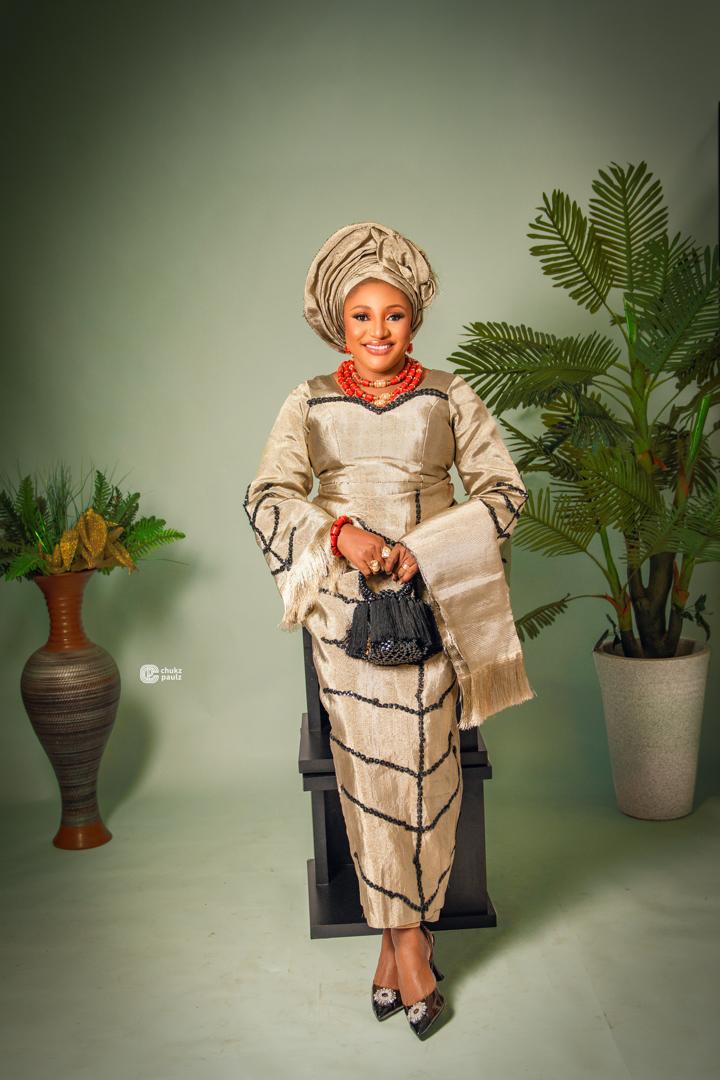 Gold traditional George attire with black detailing, matching gele and red coral beads