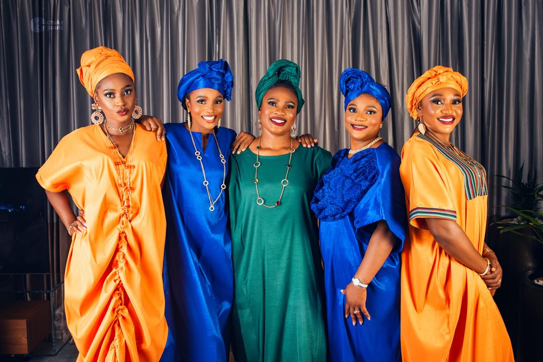 Five women in coordinated gold, royal blue and emerald gowns with matching headwraps
